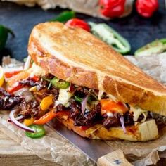 a sandwich with meat and vegetables on it sitting on top of a wooden cutting board