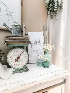 a clock sitting on top of a table next to flowers and other items in front of a window