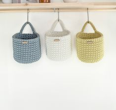 three crocheted baskets hanging on a wooden shelf in front of a white wall