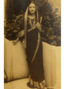 an old black and white photo of a woman dressed in native garb standing next to a planter