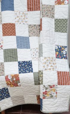 a white quilt with multicolored patchwork on the top and bottom, sitting on a chair