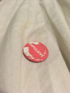 a red and white button sitting on top of a white cloth covered bed sheet with the word pleasure written across it