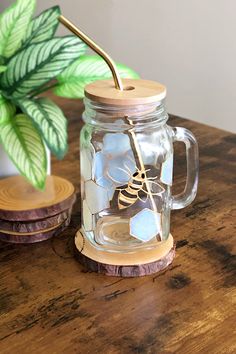 a glass jar with a wooden lid and a metal straw sticking out of it sitting on a table next to a potted plant