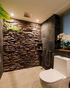 a modern bathroom with stone walls and tile flooring, along with a white toilet