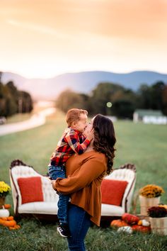 a woman holding a baby in her arms while standing next to a couch with pumpkins on it