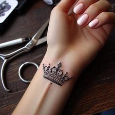 a woman's wrist with a crown tattoo on it and scissors next to her