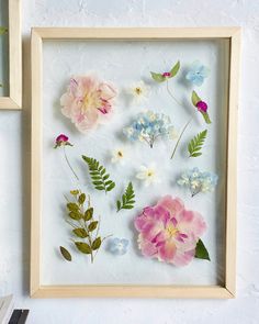 some flowers are in a wooden frame on the wall