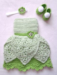 a crocheted green dress and hat with matching booties is displayed on a white surface