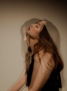 a woman with long hair standing in front of a white wall and wearing a black dress