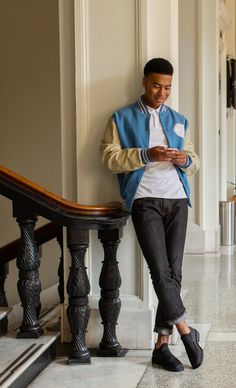 a man leaning against a wall looking at his cell phone while wearing slip ons