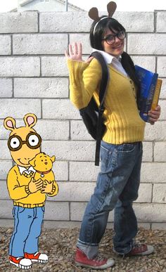 a woman in glasses and a yellow sweater is standing next to a cartoon character with her hand up