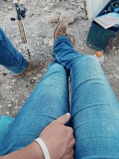 a person sitting on the ground with their legs crossed and wearing blue jeans, brown shoes