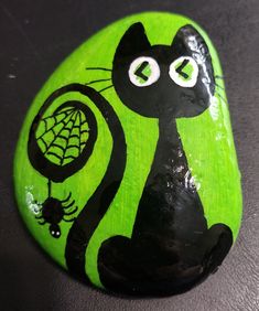 a green painted rock with a black cat and spider web on it's face