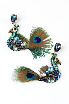 two peacock brooches with blue and green feathers on white surface next to each other