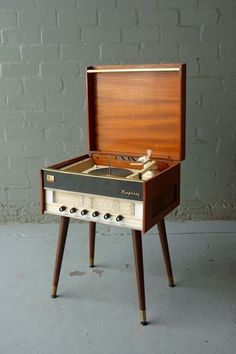 an old fashioned record player sitting on top of a wooden stand in front of a brick wall