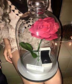 a person holding a cell phone in front of a glass vase with a flower inside