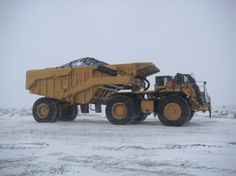 a large yellow dump truck driving down a snow covered road