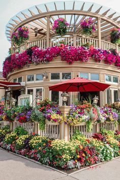 a building covered in flowers and plants with an umbrella over it's balcony area