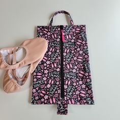 a pair of ballet shoes next to a black and pink patterned bag on a white surface