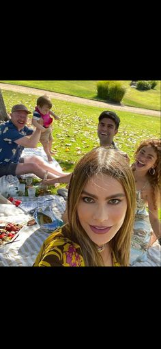 a group of people sitting on top of a blanket in the grass near a tree