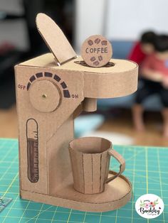 a coffee maker made out of cardboard sitting on top of a table next to a cup