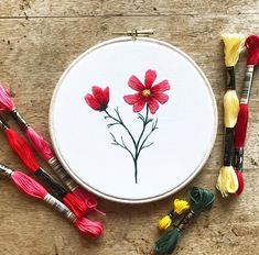 a cross stitch pattern with red flowers and tassels on a wooden table next to it