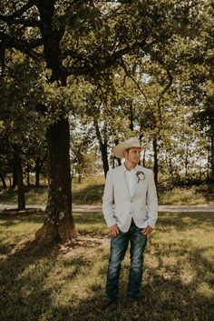 a man standing in the grass wearing a white suit and hat with his hands in his pockets