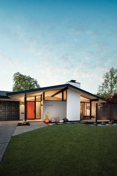 a modern house with an orange front door and black roof, on a grassy lawn