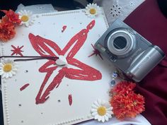 a camera sitting on top of a white card with red and yellow flowers around it