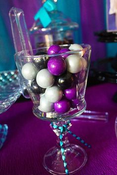 a glass bowl filled with purple and white ornaments on top of a purple table cloth