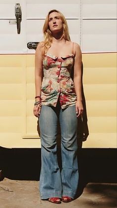 a woman standing in front of an old camper with her eyes closed and hands behind her back