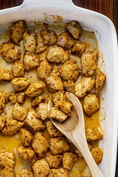 a casserole dish with chicken and gravy on the side next to a wooden spoon