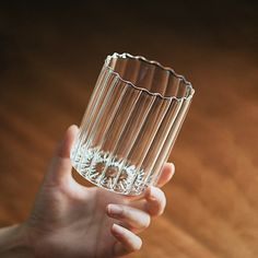 a person holding a glass in their hand on top of a wooden table with a brown surface