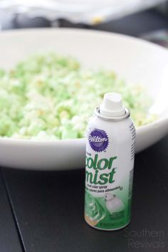 a bottle of color mist next to a bowl of green food on a black table