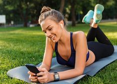 a woman is laying on the grass using her cell phone and listening to music with headphones