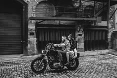 black and white photograph of two people on a motorcycle in front of an alleyway