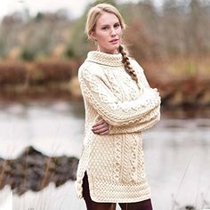 a woman standing in front of a river wearing a sweater and leggings with her arms crossed