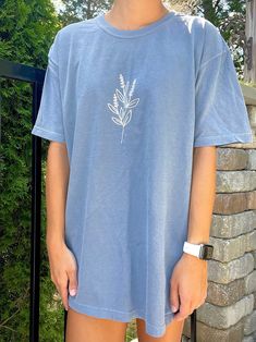 "Comfort Colors blue t-shirt with a flower in white. T-Shirt Color: Comfort Colors \"blue jean\" ✰ MODEL INFO: ✰ Height: 5'4\" Size: modeling a large. (Normally wears a small). *SIZE UP FOR AN OVERSIZED LOOK* ★ MATERIAL: ★ 100% cotton Unisex/Adult sizing." Trendy Light Blue Spring T-shirt, Casual Blue Denim T-shirt, Casual Denim Blue Short Sleeve T-shirt, White Denim Short Sleeve Top, White Short Sleeve Denim Tops, Denim Blue Crew Neck Top For Spring, Blue Denim T-shirt Relaxed Fit, Trendy Blue Denim T-shirt, Trendy Washed Blue T-shirt For Summer