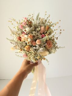 a person holding a bouquet of flowers in their hand with pink ribbon on the side