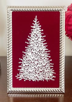 a christmas tree made out of buttons on a red and silver frame with flowers in the background