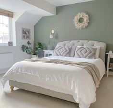 a white bed sitting in a bedroom next to a window with a wreath on the wall