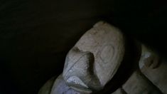 a carved wooden object sitting on top of a black floor next to a wall with writing on it