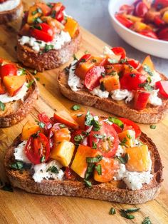 four pieces of bread with various toppings on them sitting on a wooden cutting board