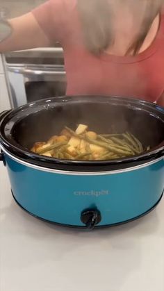 a woman is cooking green beans in an electric crock pot on the stovetop