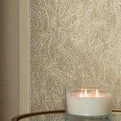 a lit candle sitting on top of a glass table next to a wallpapered wall