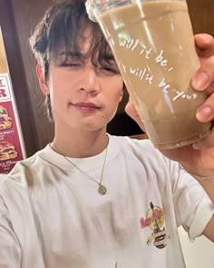 a young man holding up a glass of liquid in front of his face while looking at the camera