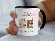 a person holding a white and black coffee mug with two pictures of houses on it