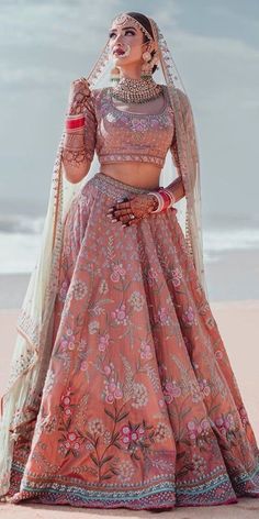 a woman in a pink lehenga standing on the beach