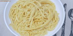 a white bowl filled with pasta on top of a table next to utensils