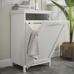 a white cabinet with towels in it next to a potted plant